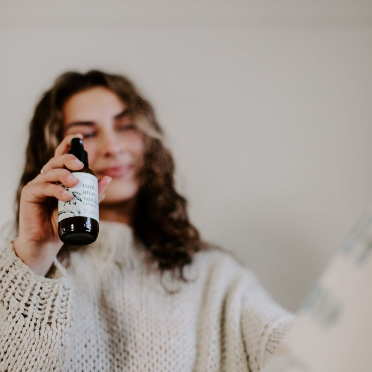 4oz Cardamom Vanilla linen spray being sprayed by women in cream sweater