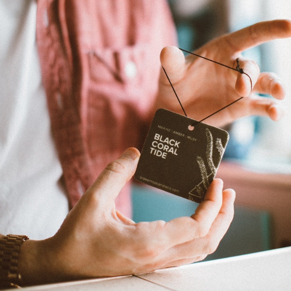 Black Coral Tide Car Freshener being held by two hands.