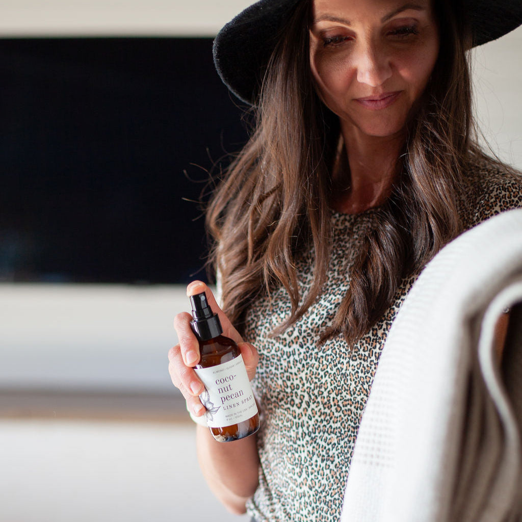 4oz Coconut Pecan Linen Spray being sprayed by a woman.