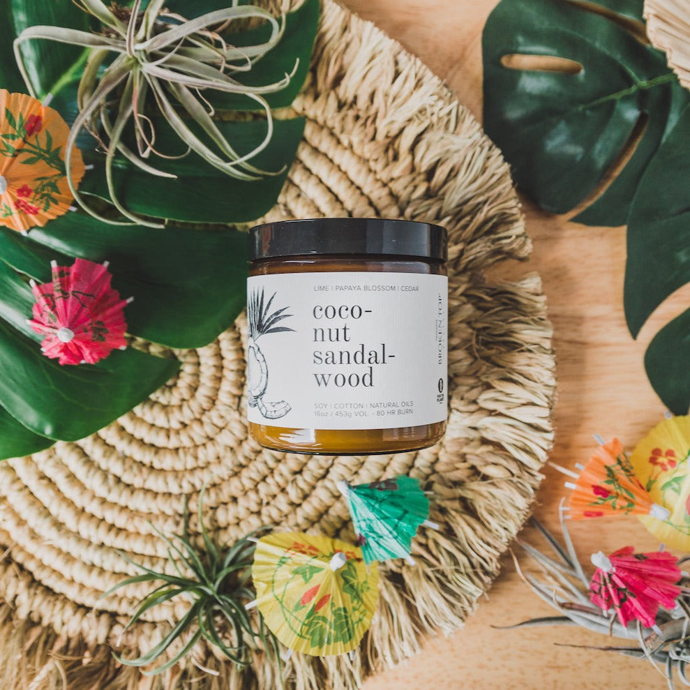 16oz Coconut Sandalwood candle on coaster surrounded by tropical drink umbrellas
