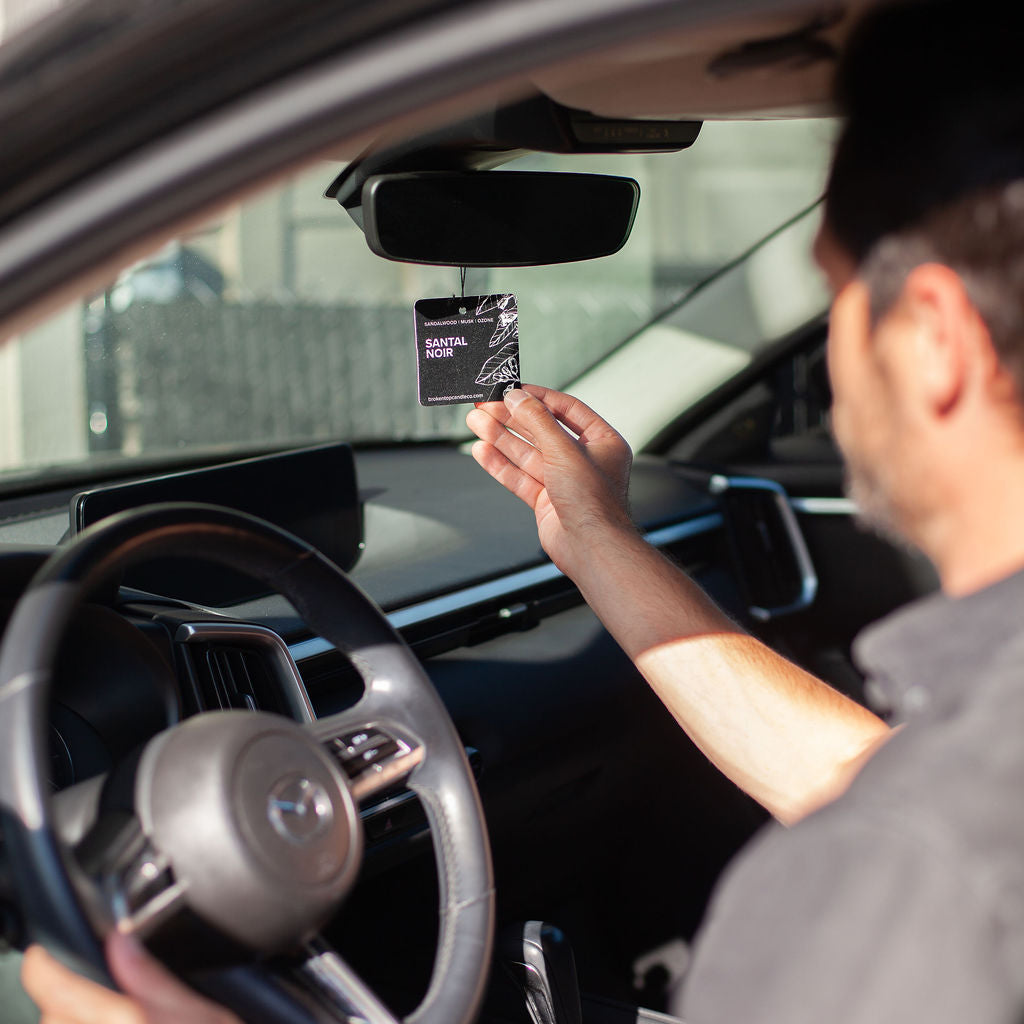 Santal Noir Car Freshener being placed on rearview mirror by a man.