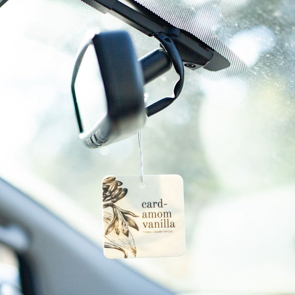 Cardamom Vanilla Car Freshener hanging from rear view mirror.