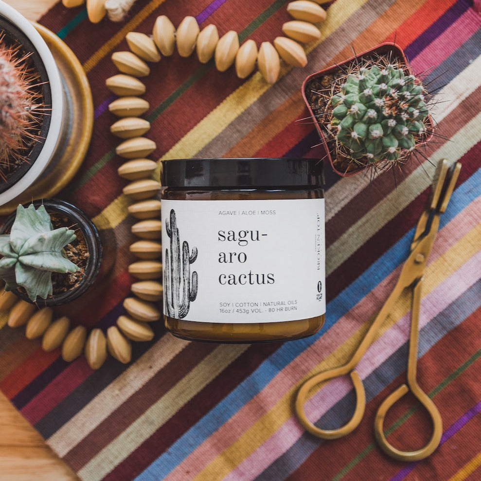 16oz Saguaro Cactus candle on stripped cloth surrounded by snuffer, cactus and wooden beads