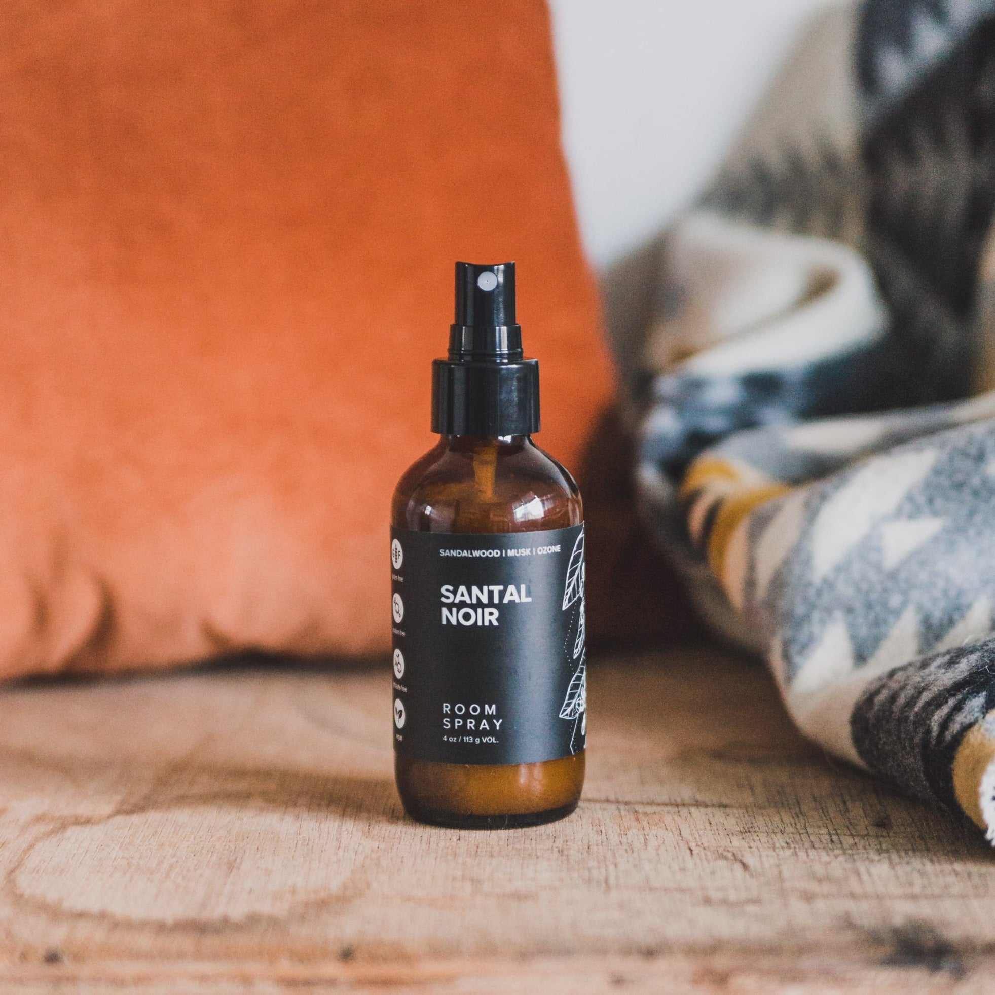 4oz Santal Noir linen spray on wood table next to a blanket