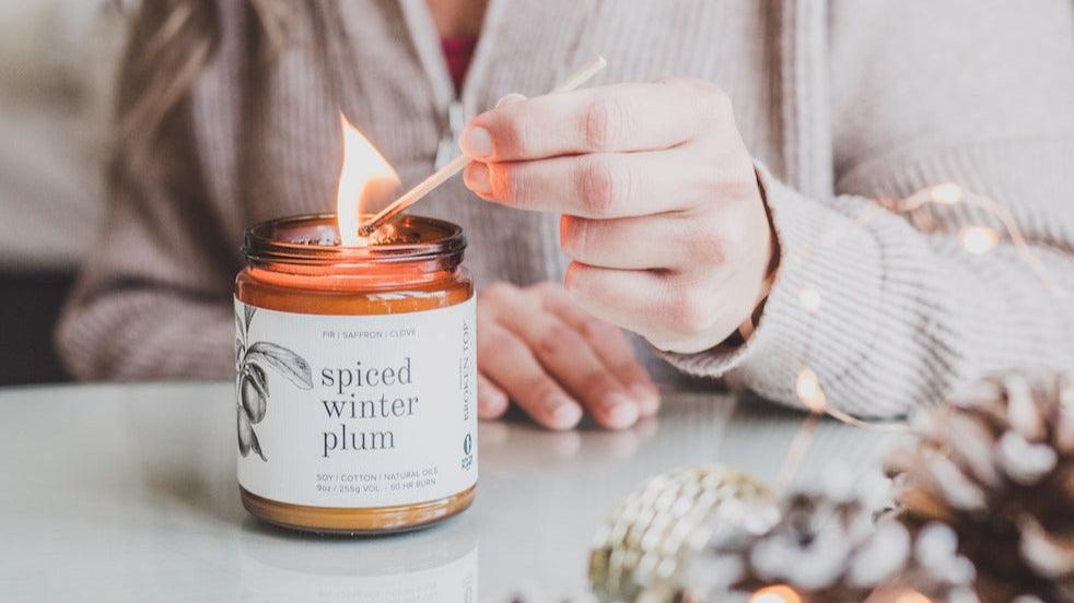 9oz Spiced Winter Plum candle being lit by women on white table