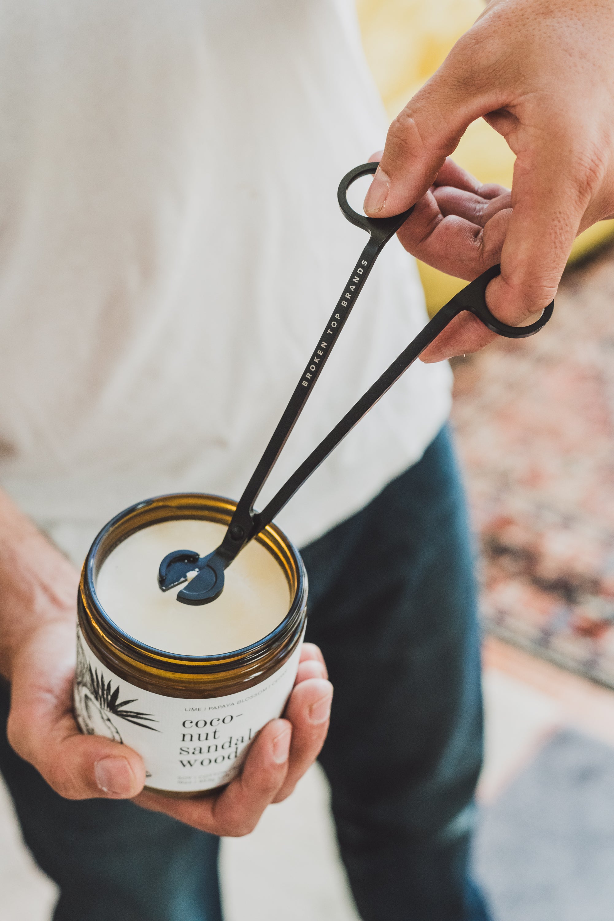 Black Broken Top Brands wick trimmer being held in man's hand and cutting wick