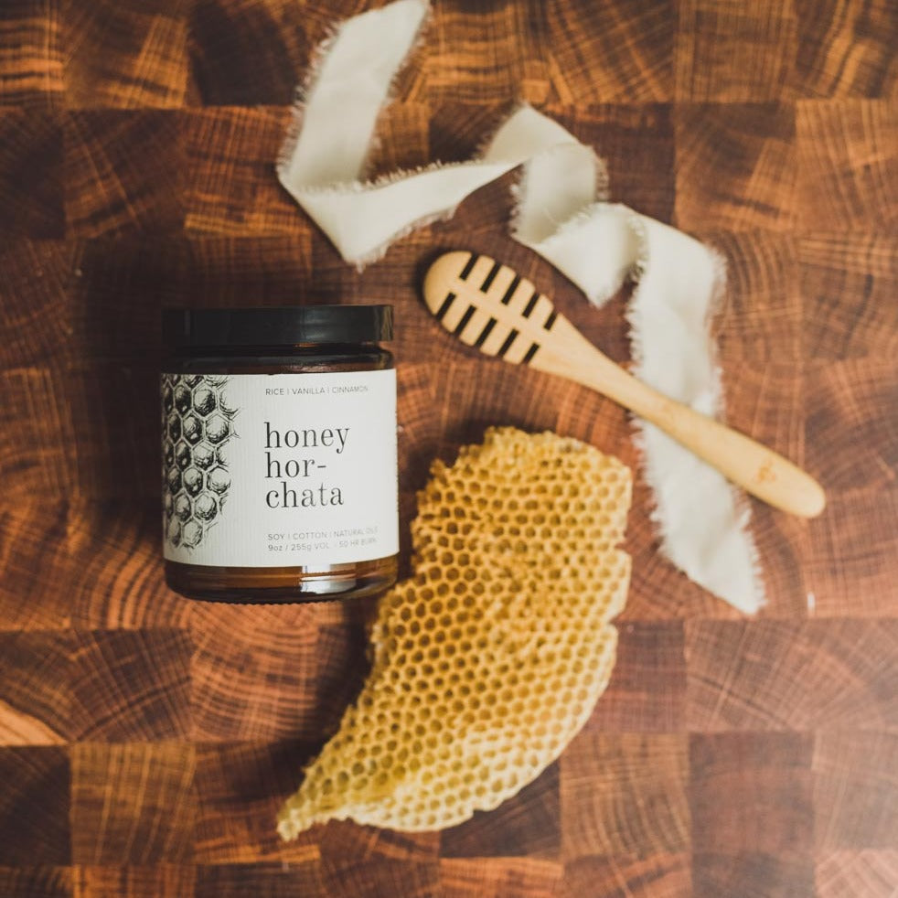 9oz Honey Horchata candle on wooden table next to honey comb and wooden spoon