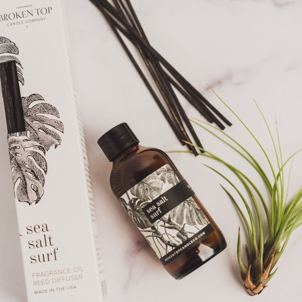 Sea Salt Surf Reed diffuser and box on white marble next to green foliage
