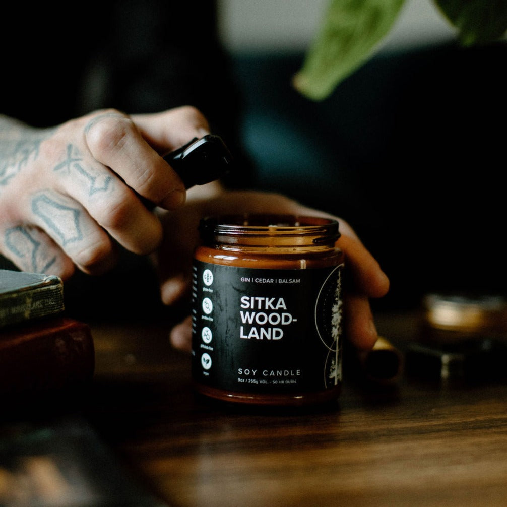 9oz Sitka Woodland candle being lit on wood table and man's hands
