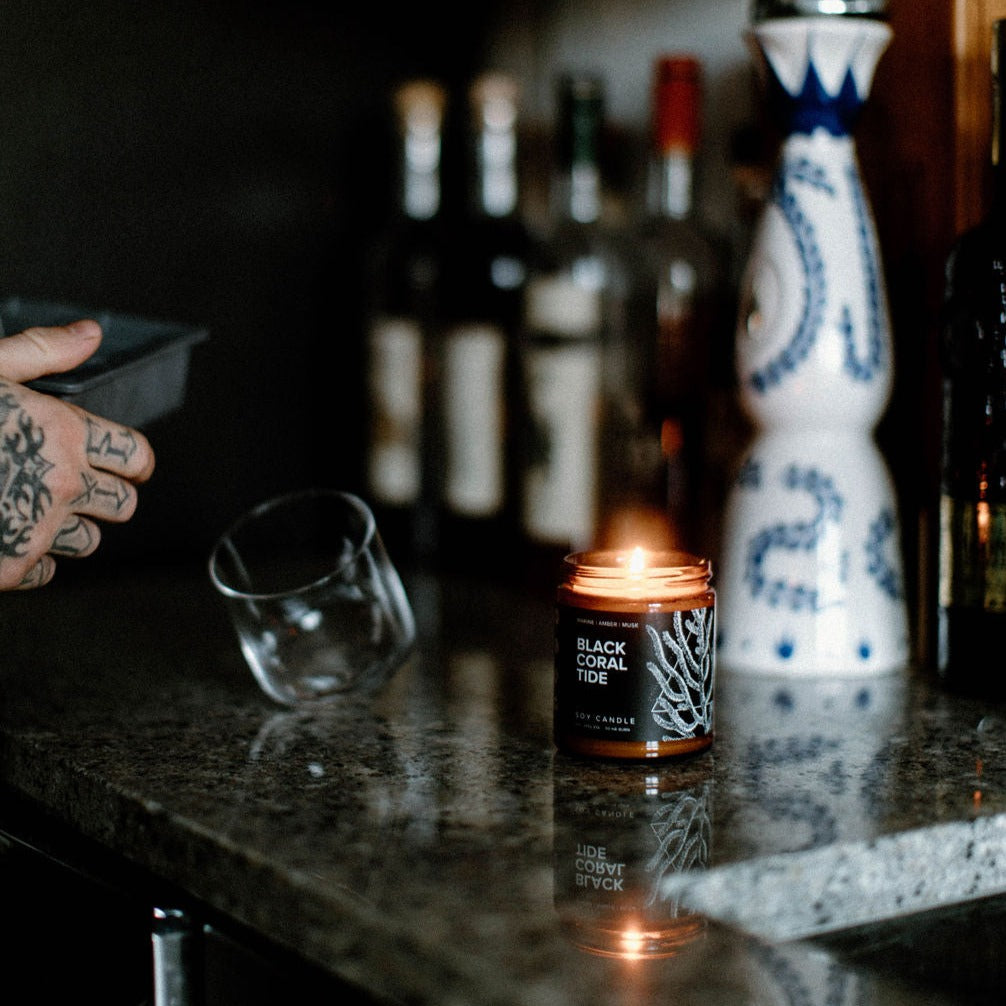 9oz Black Coral Tide candle on a bar in front of bottles and a glass