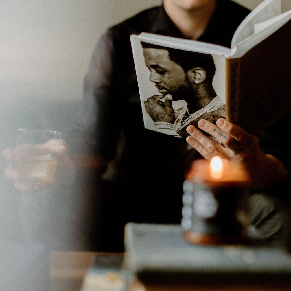 9oz Birch Charcoal candle on a coffee table in front on a tattooed man reading a Meek Mill book