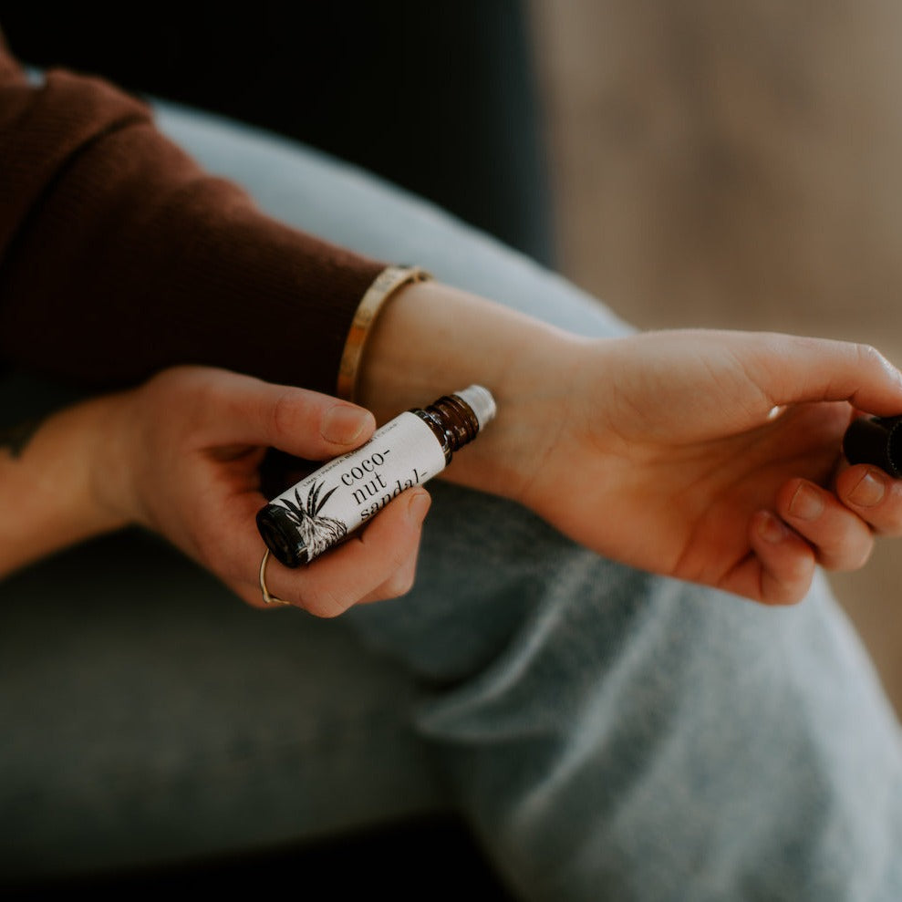 Coconut Sandalwood roll-on perfume being held and applied to women's wrist