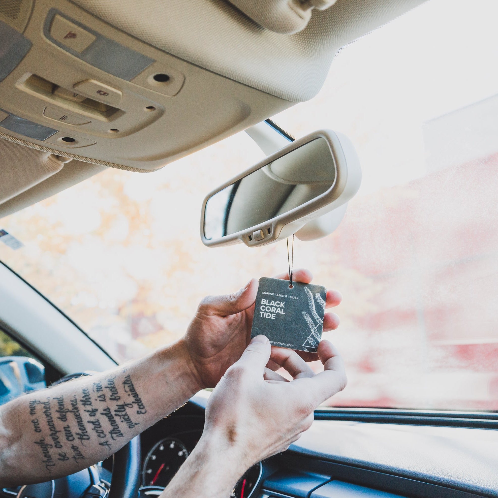 Black Coral Tide car freshener hanging on rearview car mirror with man's hands