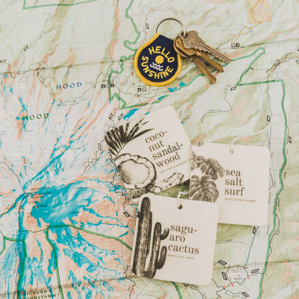 Coconut Sandalwood car freshener on map next to keys and two other car fresheners.