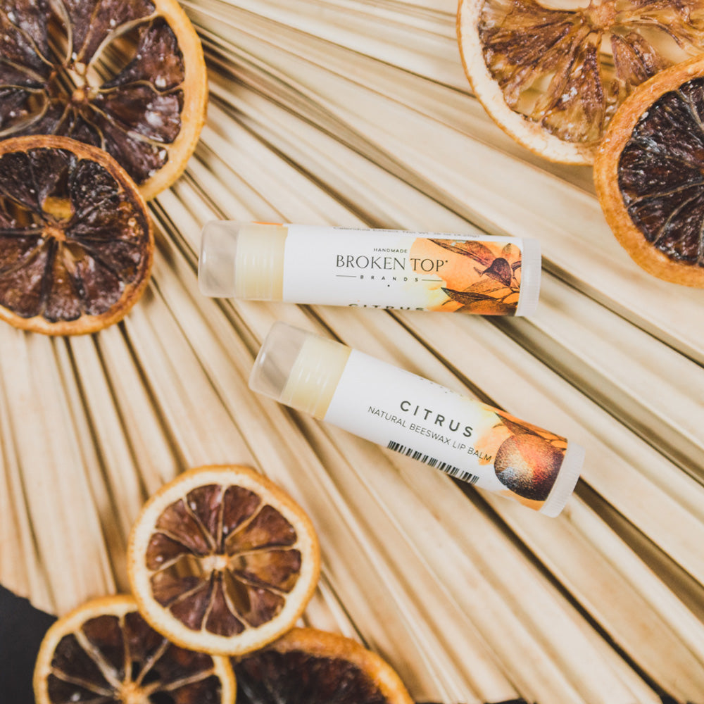 Two Citrus lip balms on palms surrounded by dried citrus