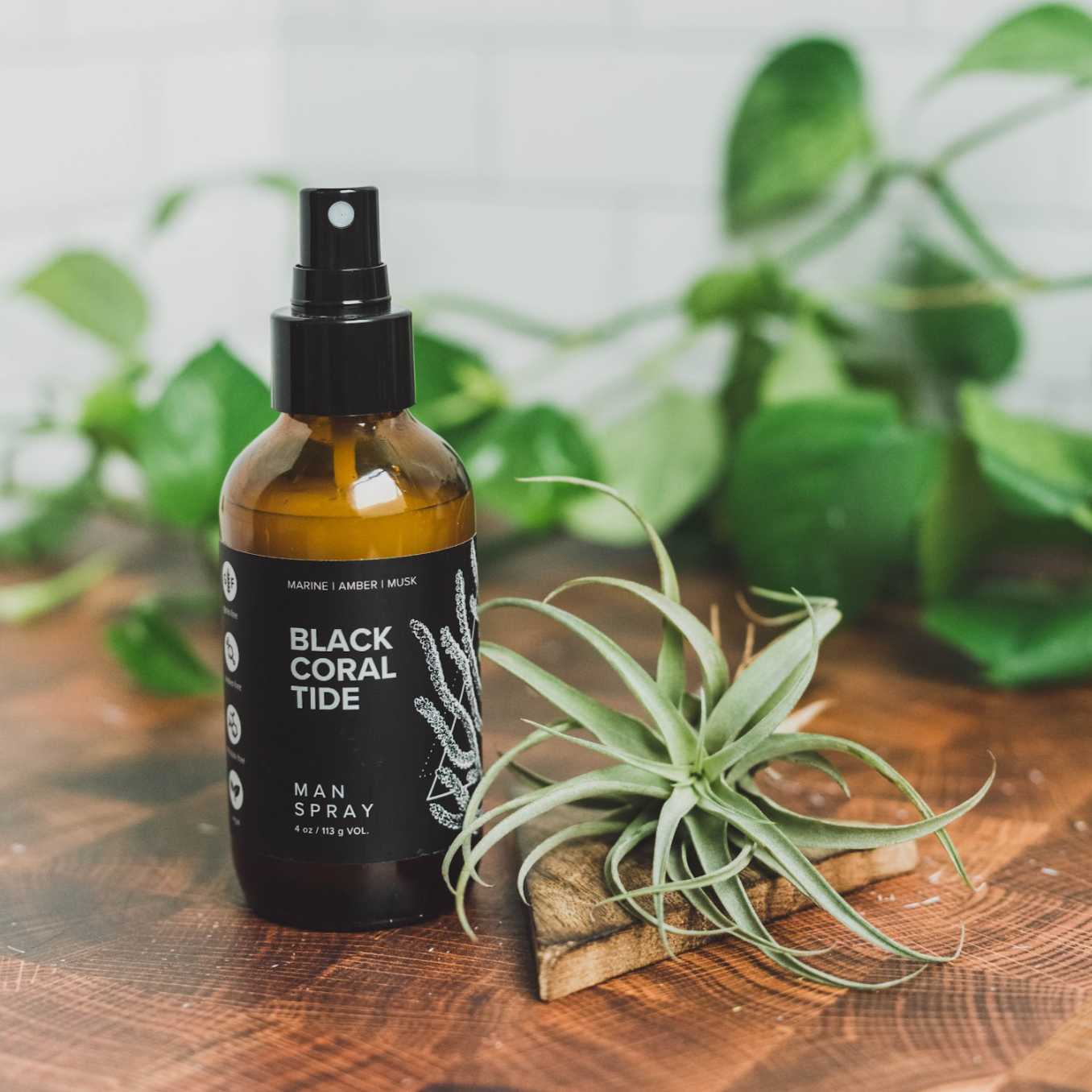 4oz Black Coral Tide linen spray on wood table next to green foliage