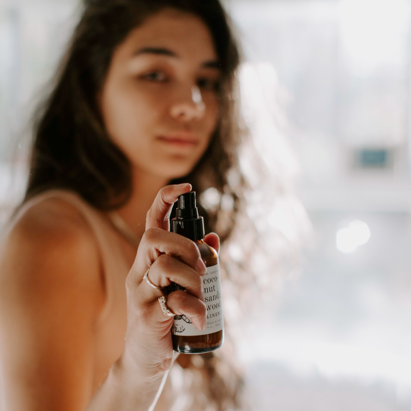 4oz Coconut Sandalwood linen spray being sprayed by women