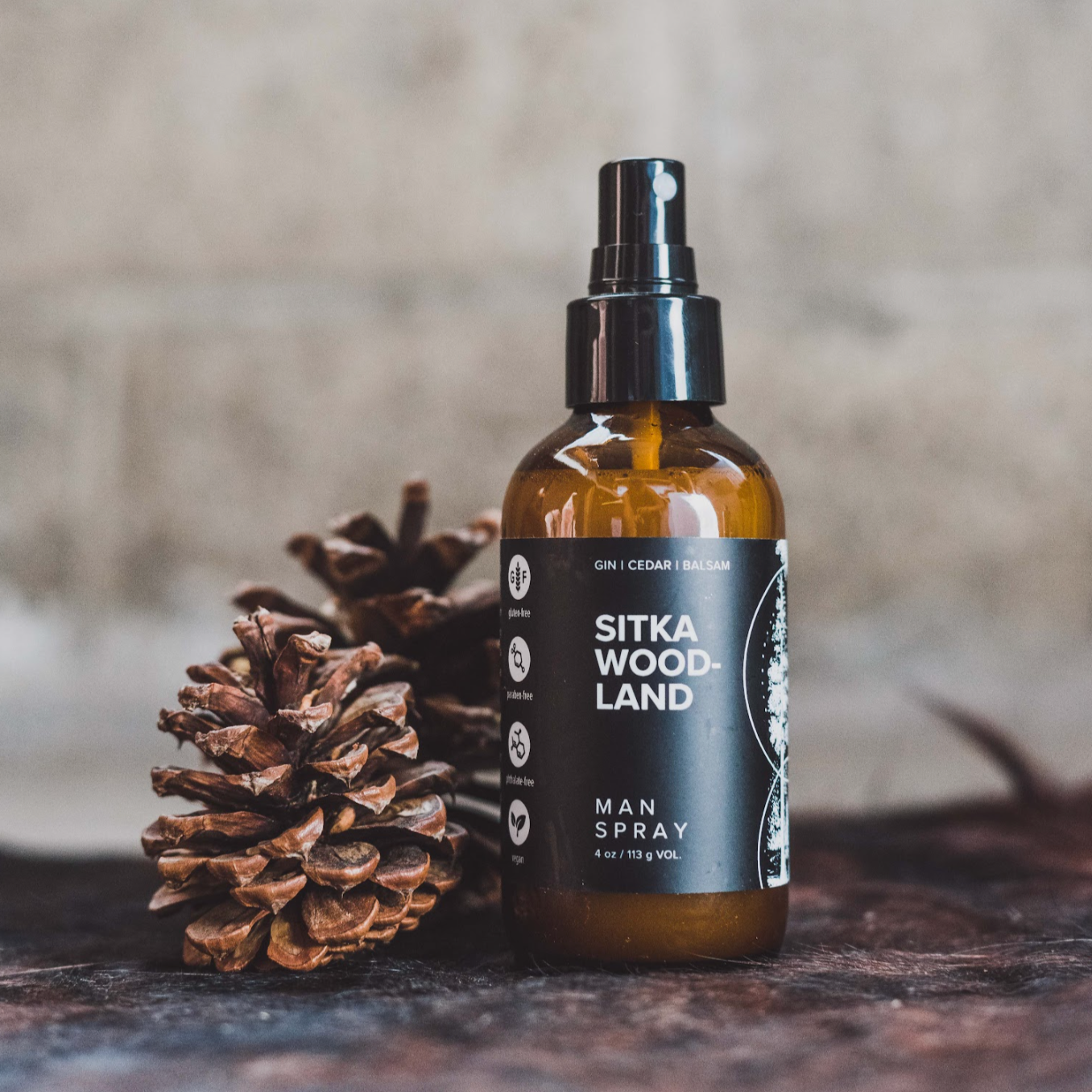 4oz Sitka Woodland spray on wood next to pinecones