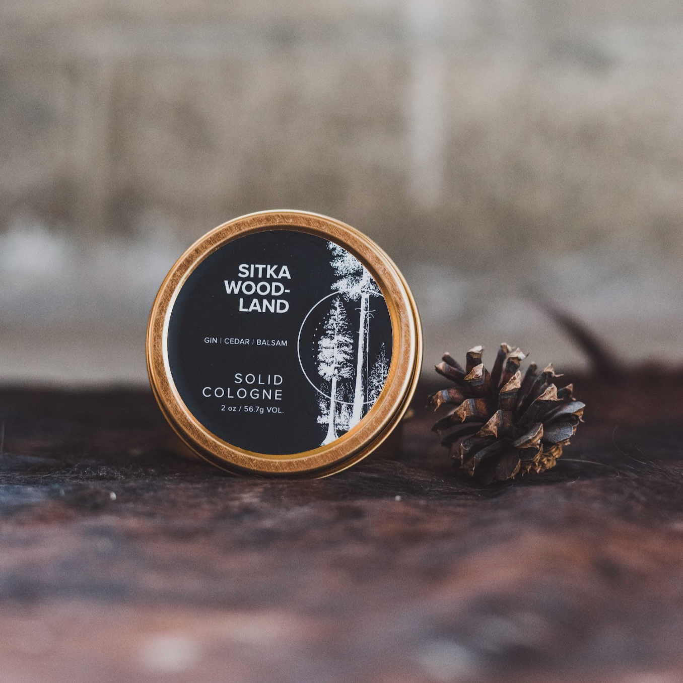 Sitka Woodland solid cologne on wood table next to pinecone