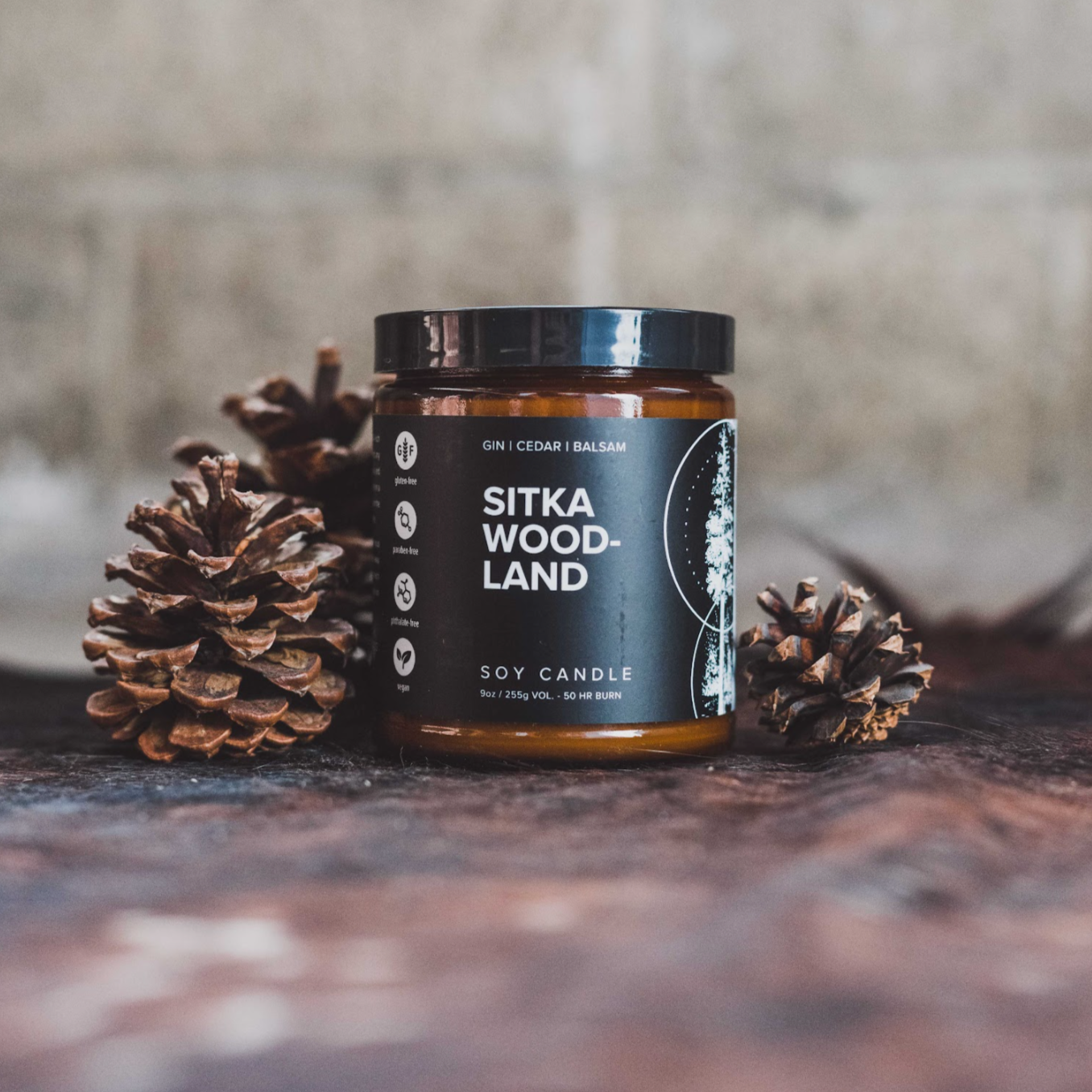 9oz Sitka Woodland candle on wood table next to three pinecones