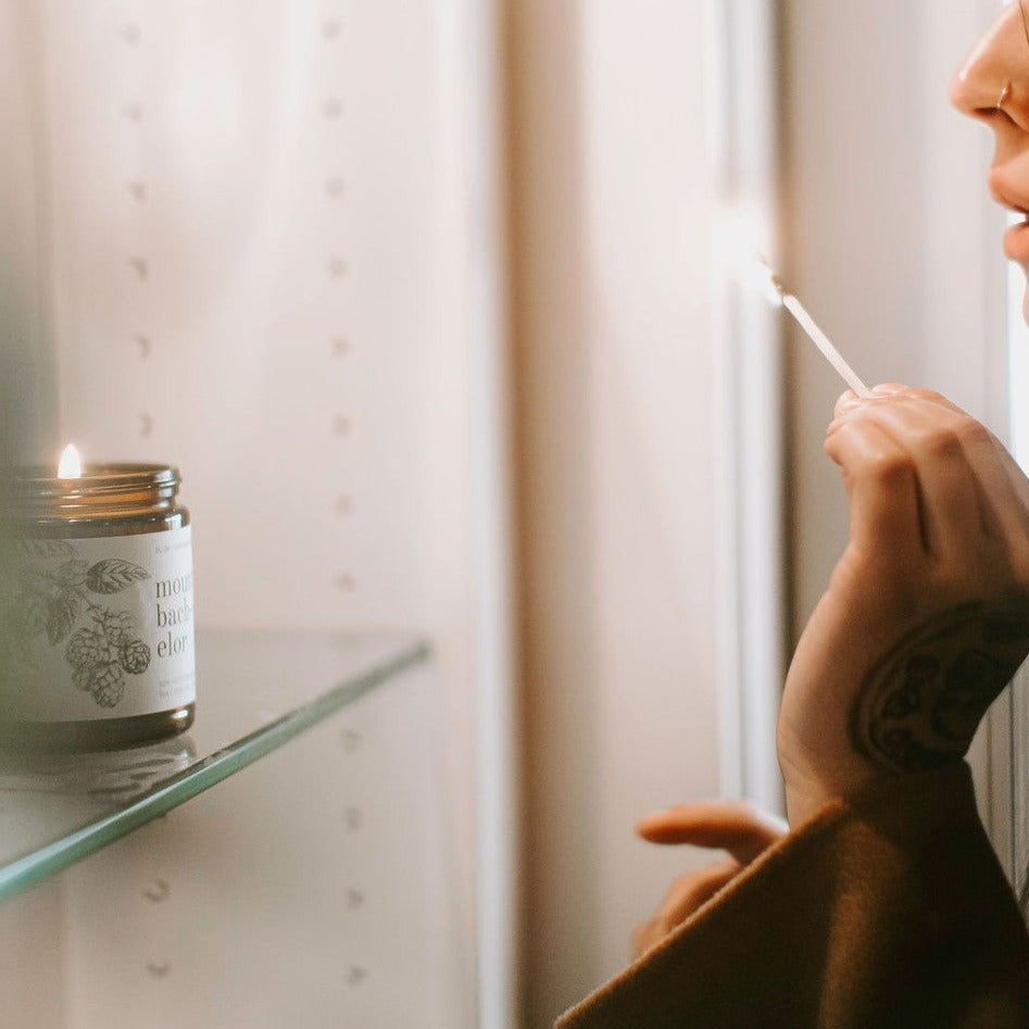 Lit 9oz Mount Bachelor candle on glass shelf with wooden match and women