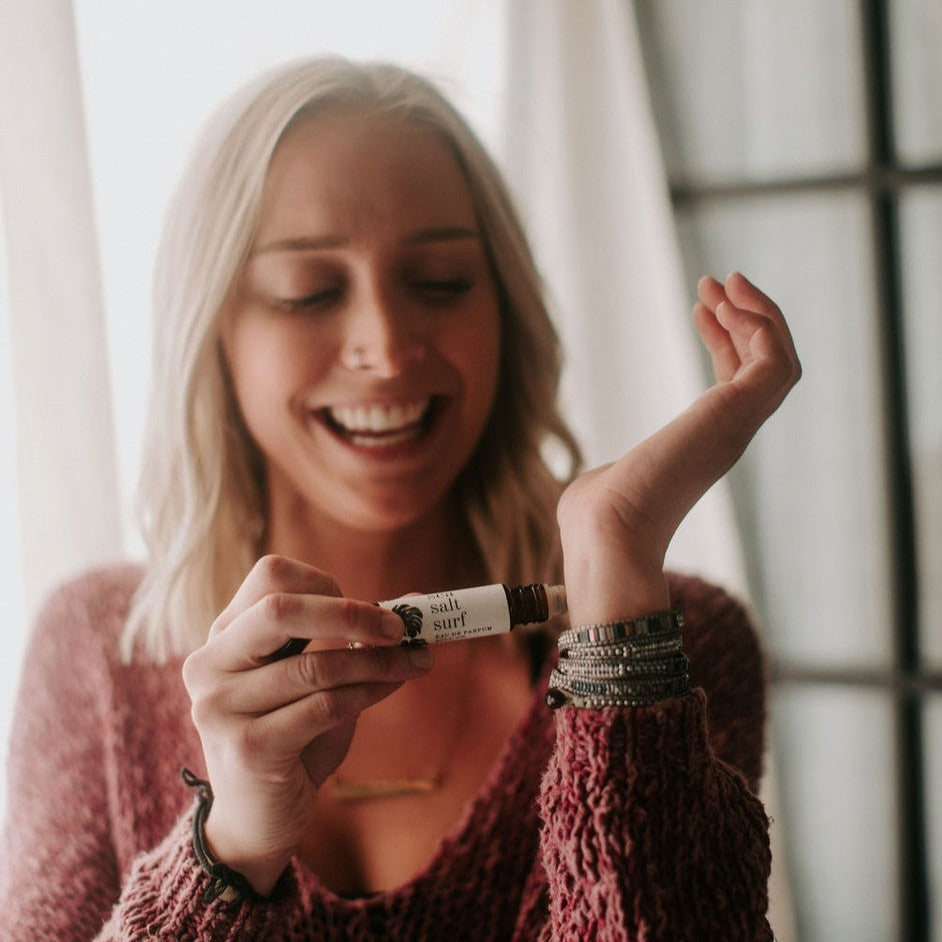 Sea Salt Surf roll-on perfume being held by smiling women and applied to her wrist