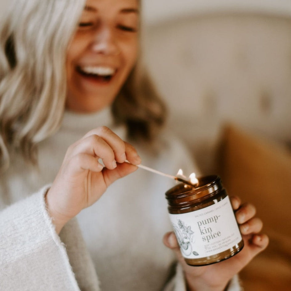 9oz Pumpkin Spice candle being held by laugh women and lit by wooden match