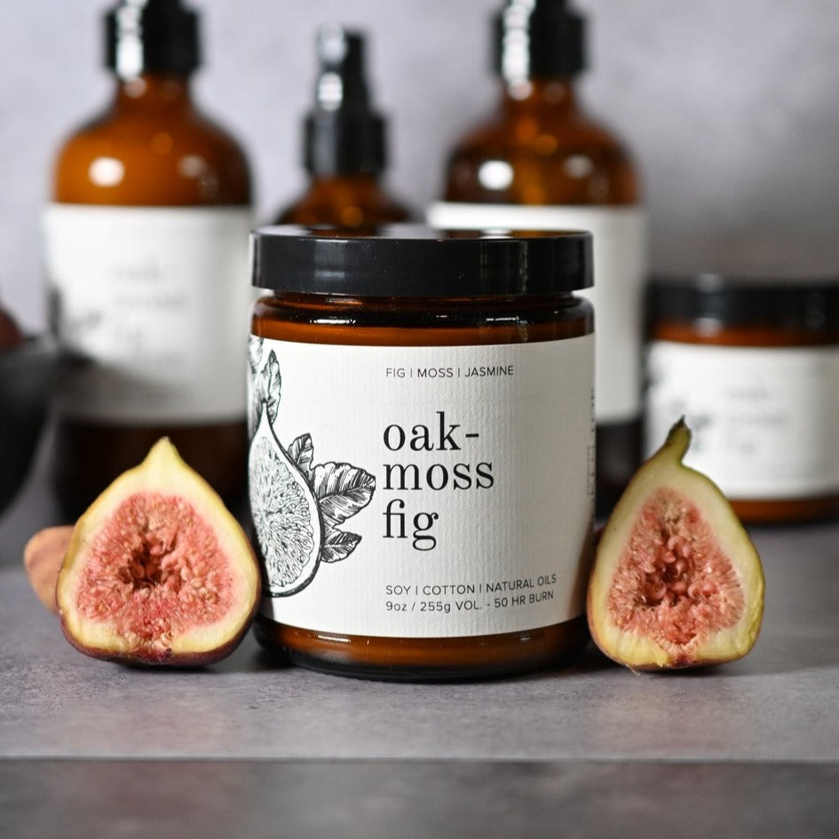 9oz Oakmoss Fig candle on grey counter next to two figs