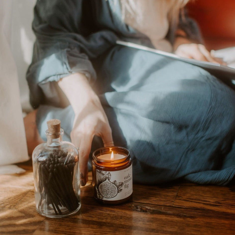 9oz Oakmoss Fig candle wooden floorboards next to match vase and women
