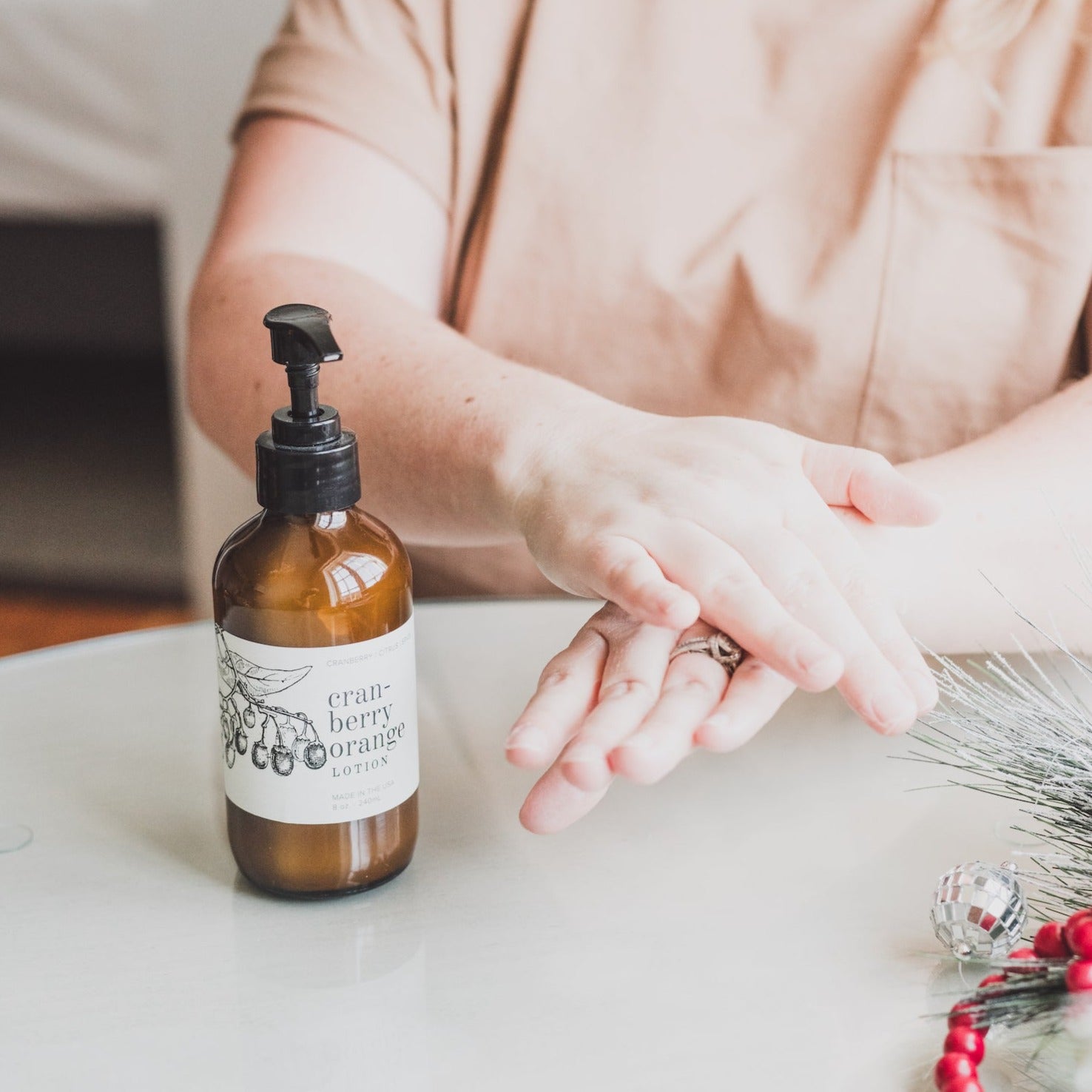 Cranberry Orange 8oz lotion on table with women's hands