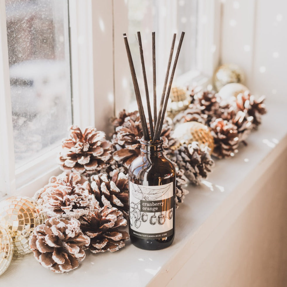 Cranberry Orange Reed diffuser on window seal next to pinecones