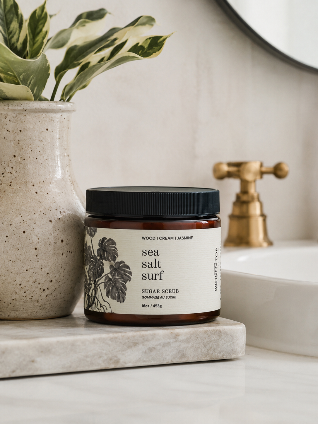 16oz Sea Salt Surf Sugar Scrub on white marble counter with sink and plant in background