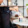 Young woman lighting 9oz 'Sweet Rain' Soy Candle on white table