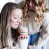 Woman in white sweater smelling 9oz 'Ain't No Hood Like Motherhood' Soy Candle with young woman in background