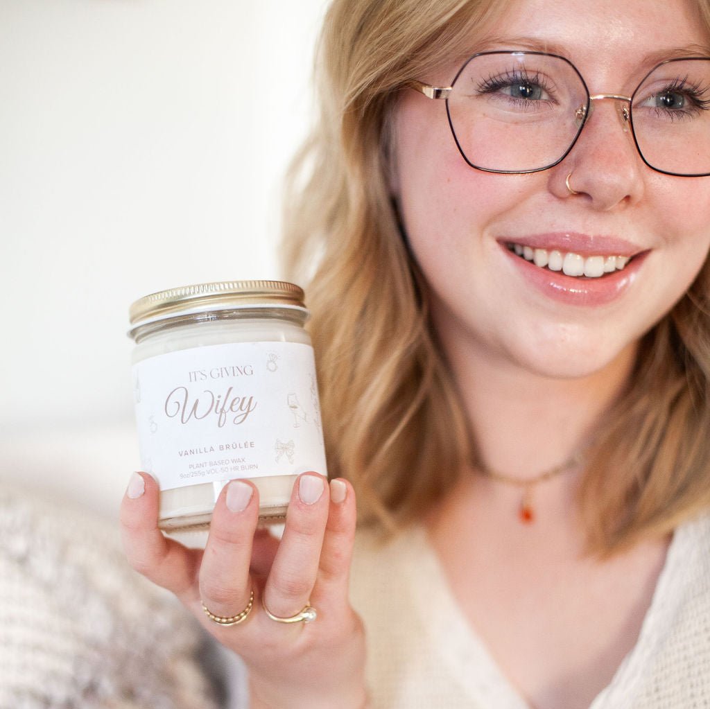 Young woman smiling, holding up 9oz 'Its Giving Wifey' Soy Candle