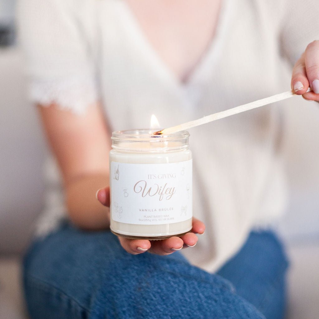 Woman holding lit match, lighting 9oz 'Its Giving Wifey' Soy Candle while sitting