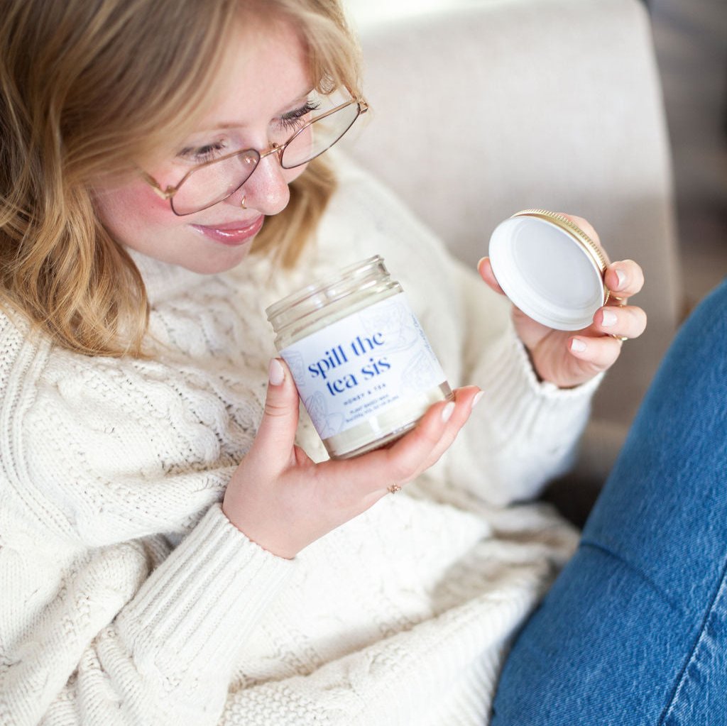 Young woman holding open 9oz 'Spill The Tea Sis' Soy Candle and smelling