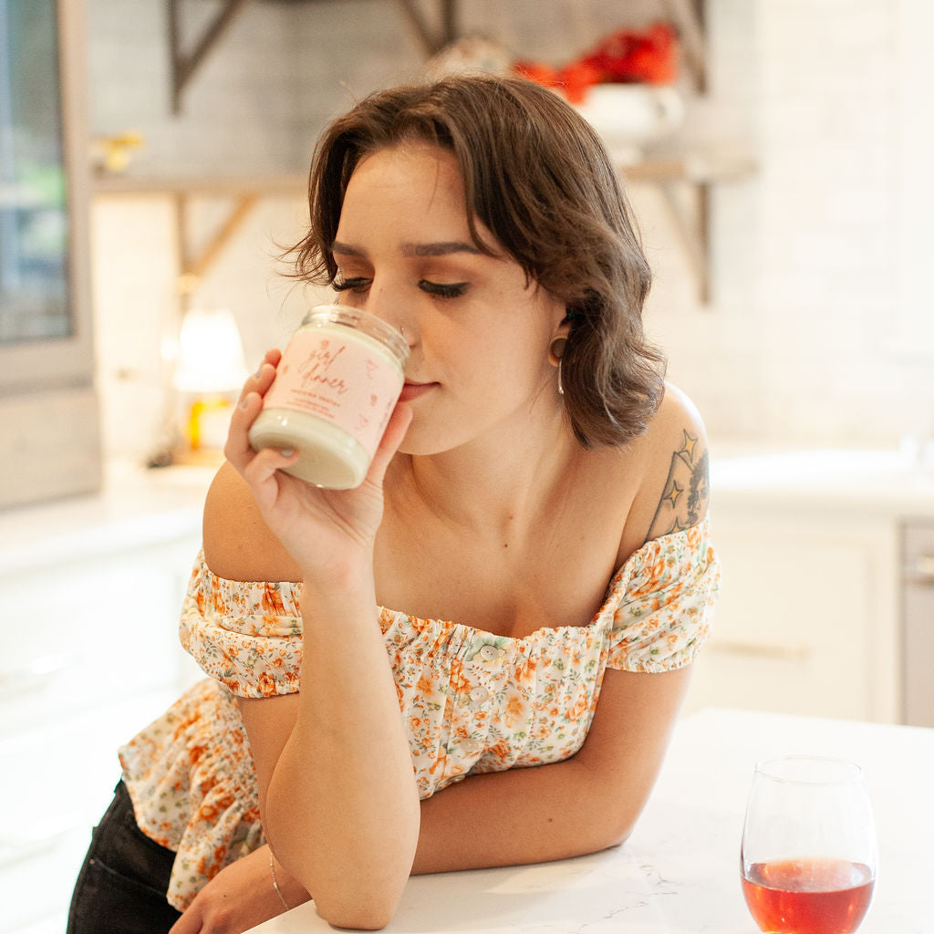 Young woman smelling 9oz 'Girl Dinner' Soy Wax Candle in kitchen