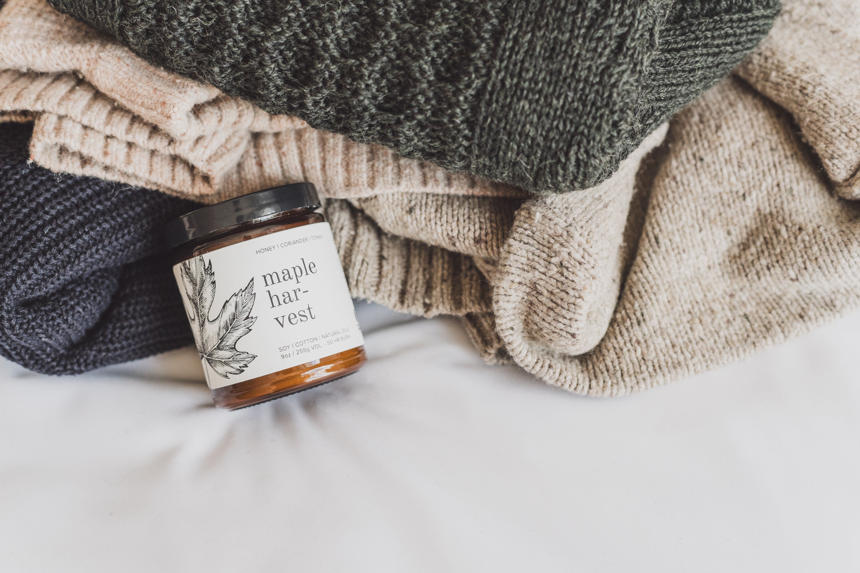 Maple Harvest 9oz candle resting on a linens and blankets