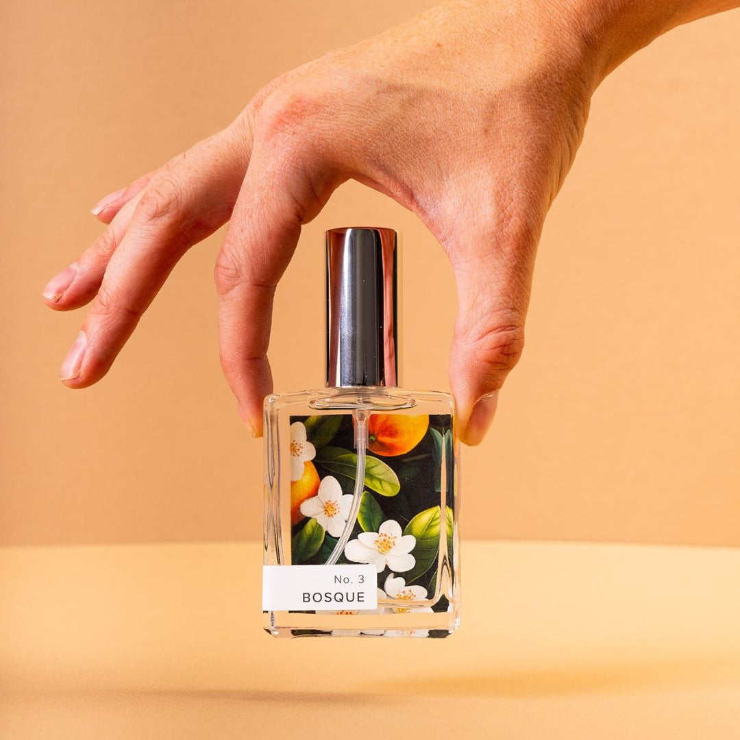 Hand holding a perfume bottle labeled 'Bosque' against a beige background