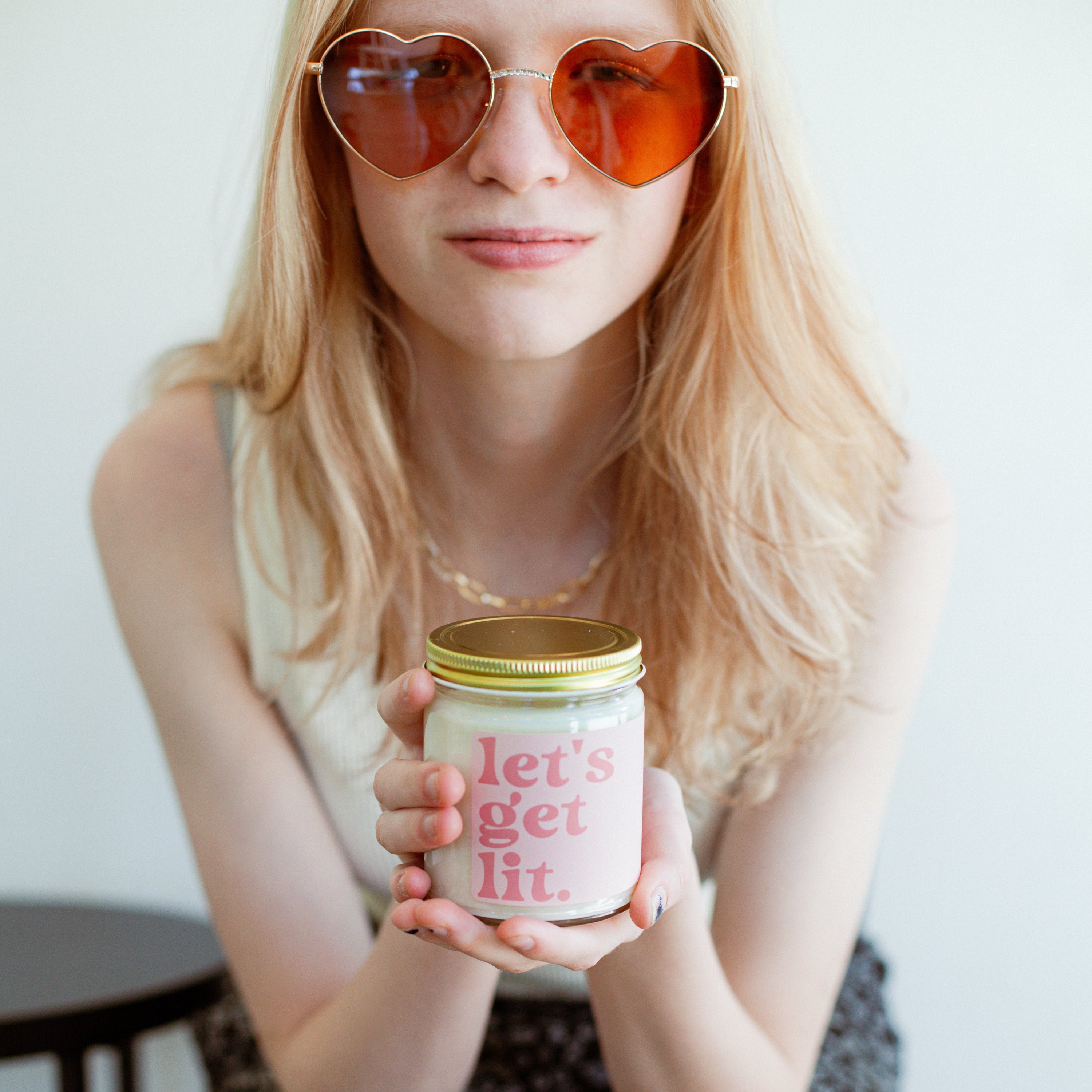 'Let's Get Lit' 9oz Soy Candle being held by a young woman wearing heart shaped sunglasses. 