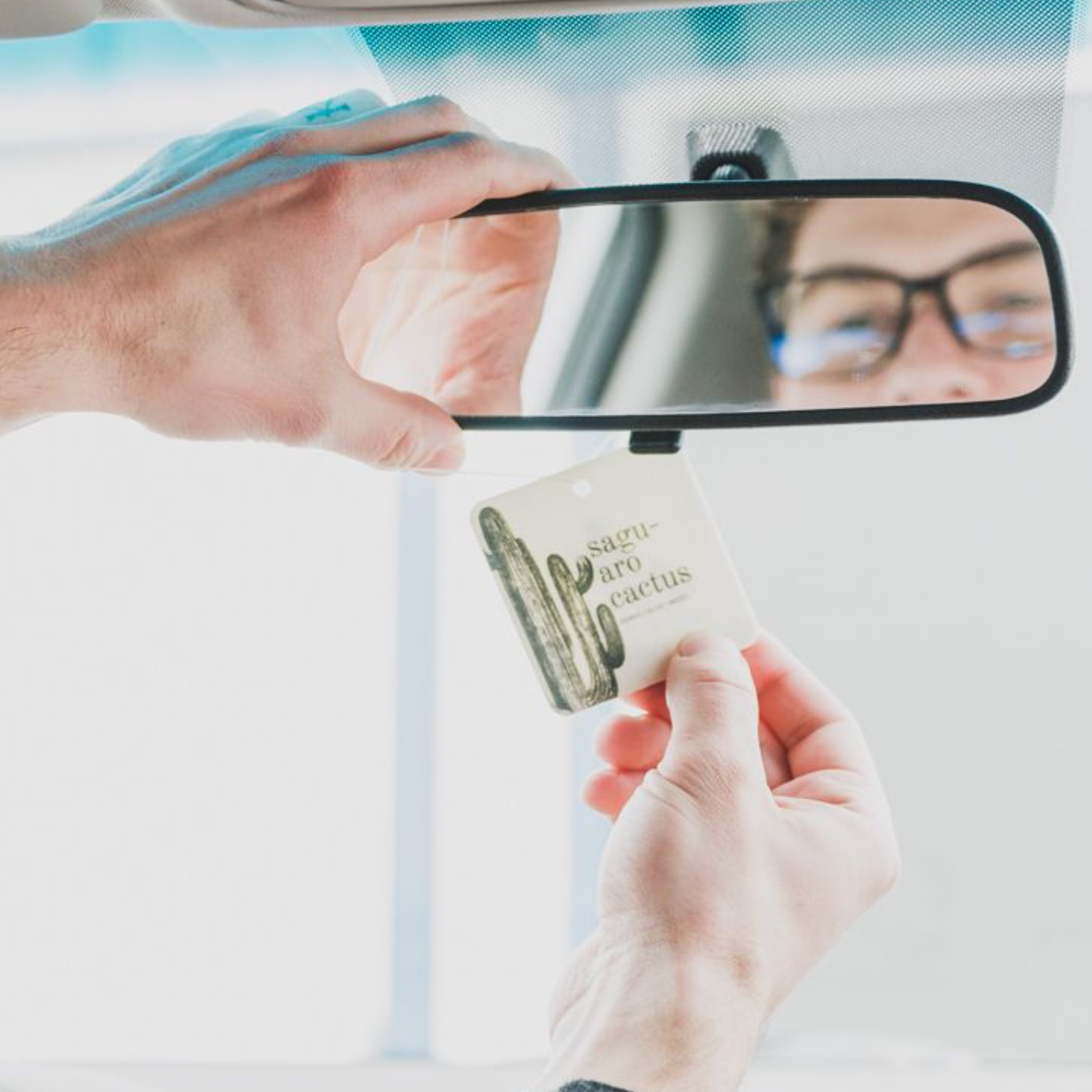 Saguaro Cactus Car Freshener being hung from a rearview mirror by two hands. 