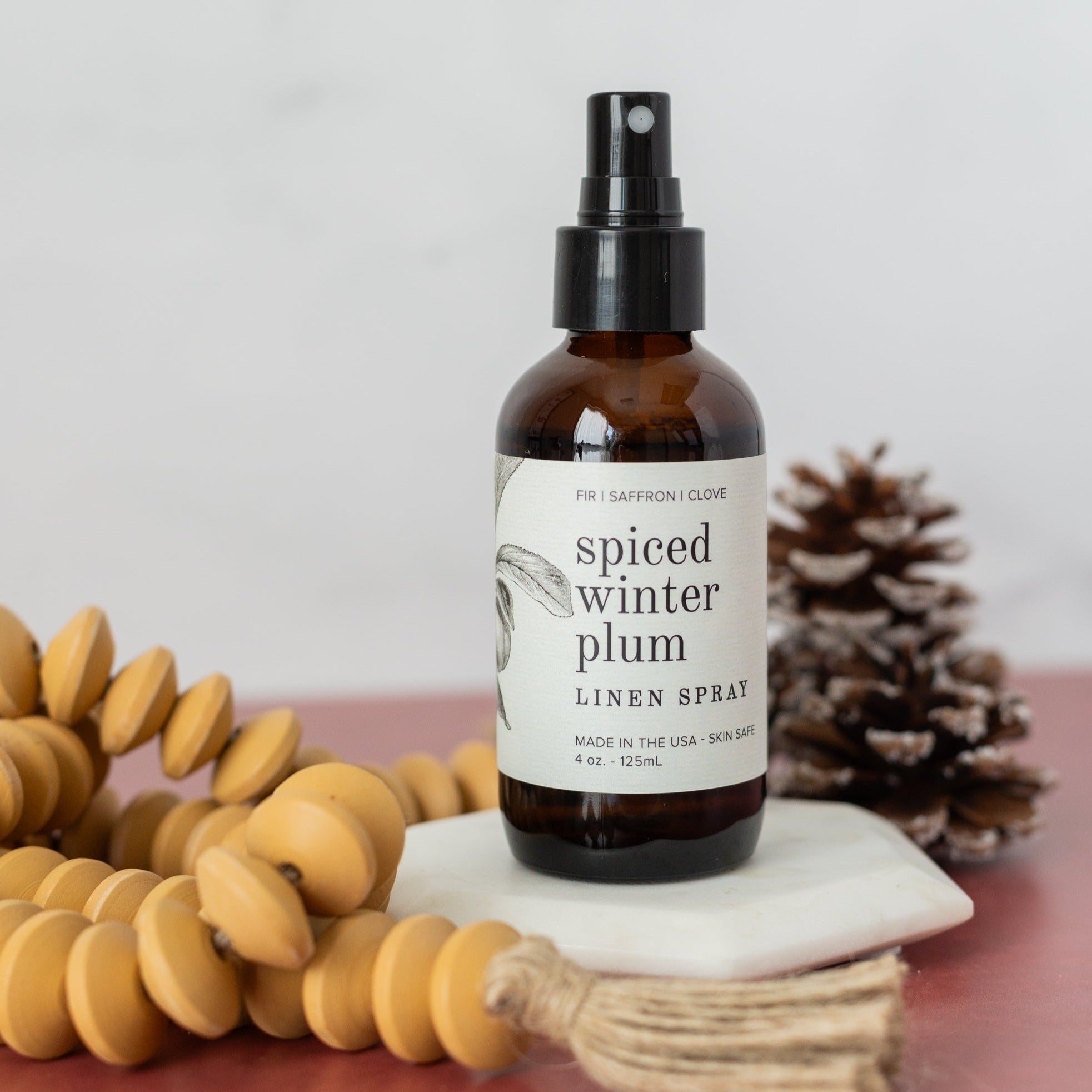 4oz Spiced Winter Plum spray on white coaster near pinecone