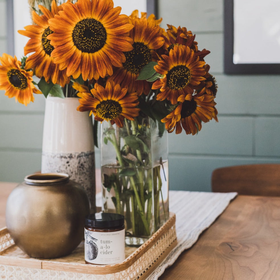 9oz Tumalo Cider candle on table next to sunflowers and vases