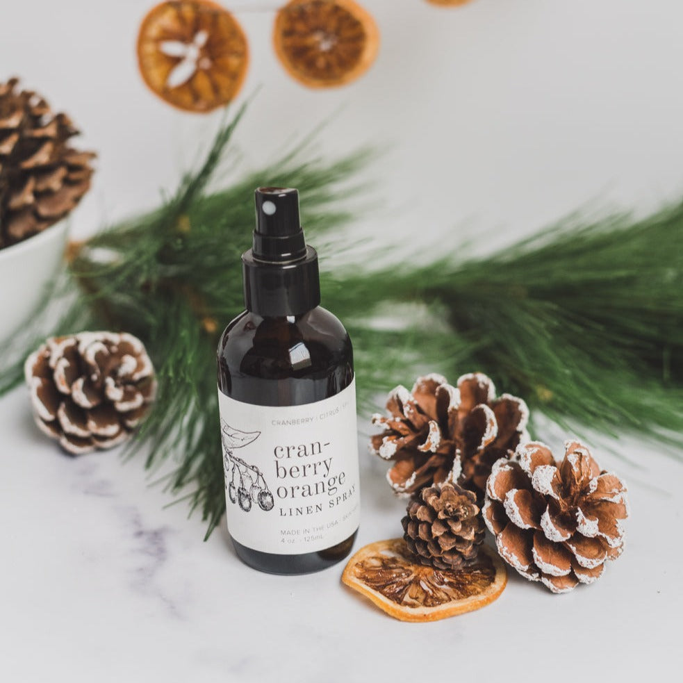 4oz Cranberry Orange linen spray on white table next to dried citrus and pinecones