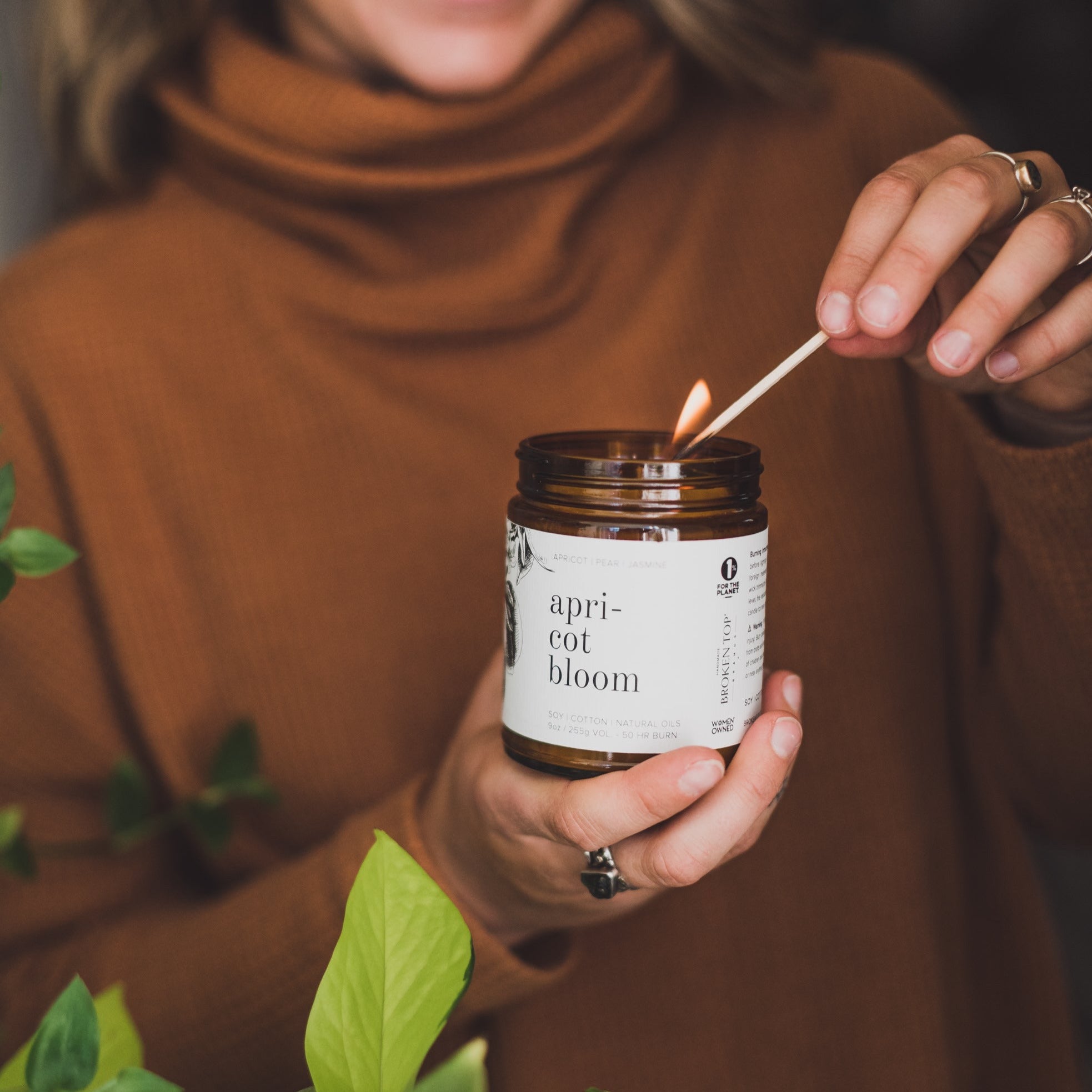 9oz Apricot Bloom Candle being held by a women in brown and lit with a wooden match