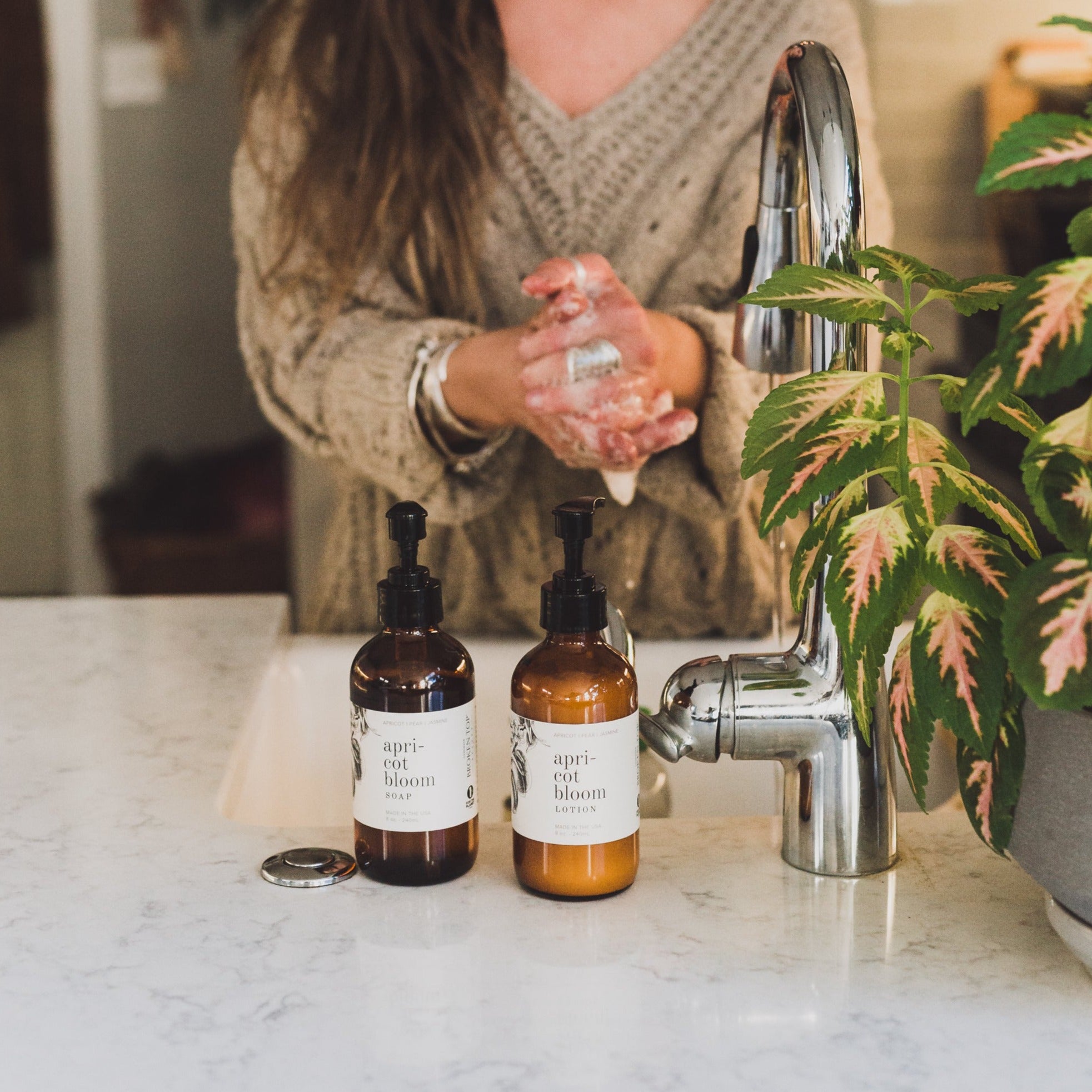 Apricot Bloom 8oz liquid soap on kitchen counter next to Apricot Bloom lotion with women in the background washing her hands